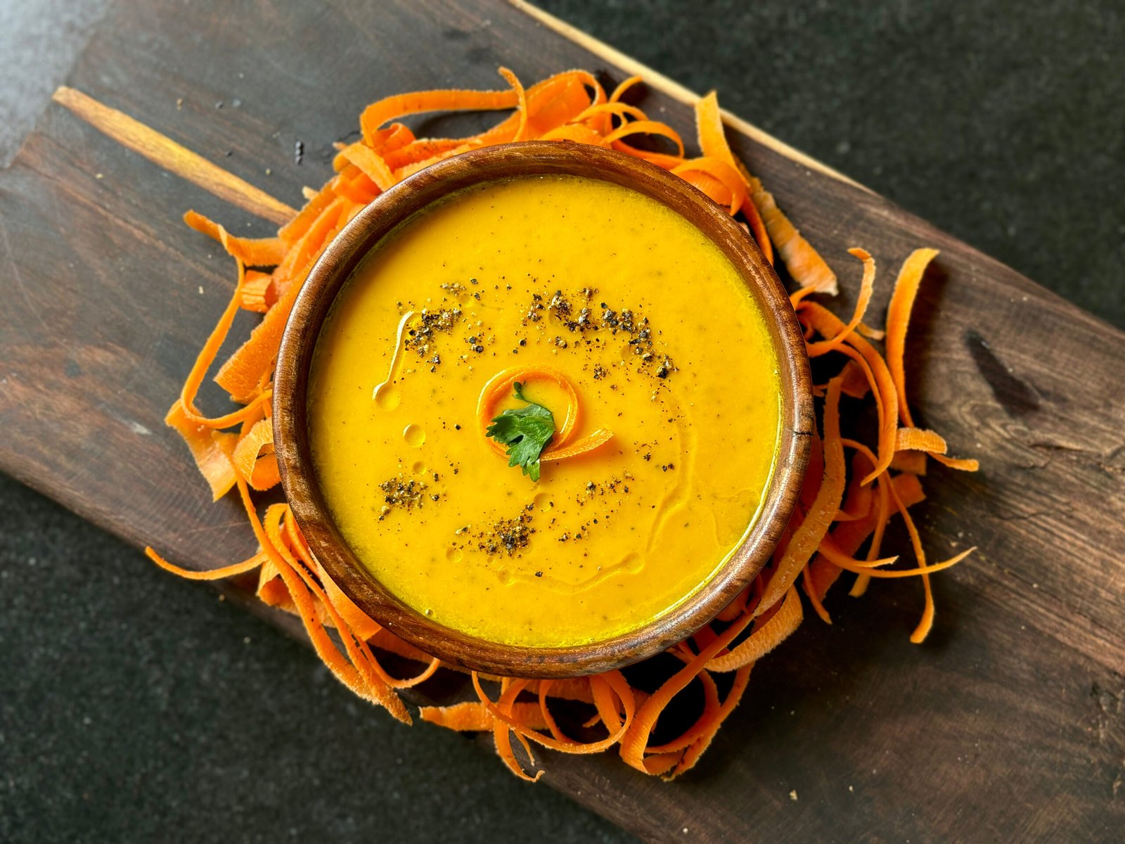 Cream of carrot soup garnished with carrot peel black pepper coriander and olive oil